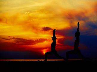 Image showing Yoga people training and meditating in warrior pose outside by beach at sunrise or sunset.