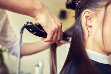 Image showing stylist with iron straightening hair at salon