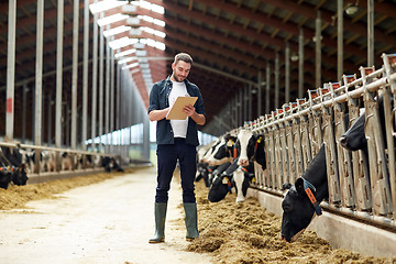 Image showing farmer with clipboard and cows in cowshed on farm