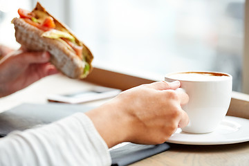 Image showing woman drinking coffee and eating sandwich at cafe