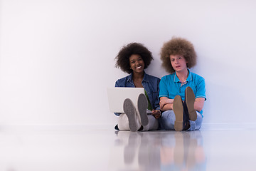 Image showing multiethnic couple sitting on the floor with a laptop and tablet