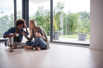 Image showing multiethnic women sit on the floor and drinking coffee