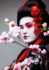 Image showing young pretty geisha in black kimono among sakura, asian ethno close up
