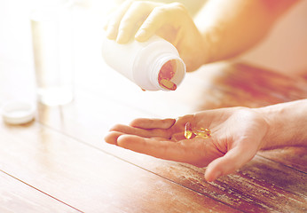 Image showing close up of man pouring fish oil capsules to hand