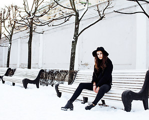 Image showing young pretty modern hipster girl waiting on bench at winter snow park alone, lifestyle people concept 