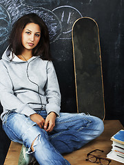 Image showing young cute teenage girl in classroom at blackboard seating on ta