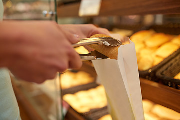 Image showing hand with tongs taking bun at bakery or grocery