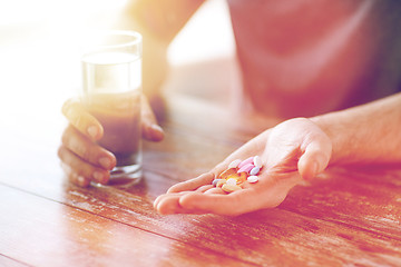 Image showing close up of male hands holding pills and water