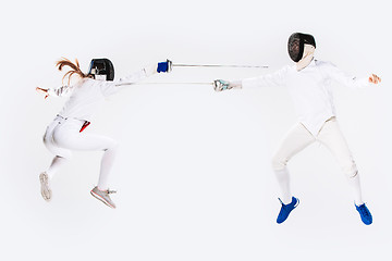 Image showing The woman and man wearing fencing suit practicing with sword against gray