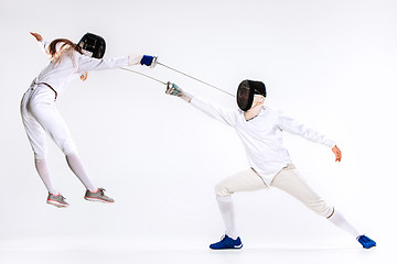 Image showing The woman and man wearing fencing suit practicing with sword against gray