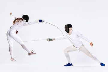 Image showing The woman and man wearing fencing suit practicing with sword against gray