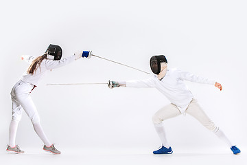 Image showing The woman and man wearing fencing suit practicing with sword against gray