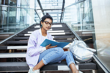 Image showing young cute indian girl at university building sitting on stairs reading a book, wearing hipster glasses, lifestyle people concept