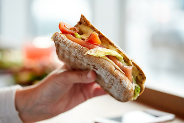 Image showing hand with salmon panini sandwich at restaurant