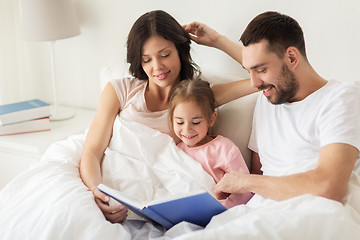 Image showing happy family reading book in bed at home