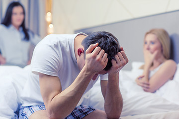 Image showing man sitting on the bed with two women on the back