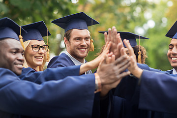 Image showing happy students in mortar boards making high five