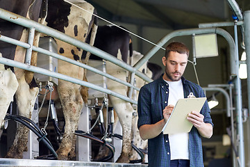 Image showing man with clipboard and milking cows on dairy farm