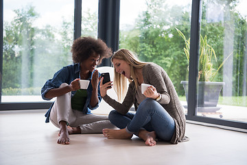 Image showing multiethnic women sit on the floor and drinking coffee