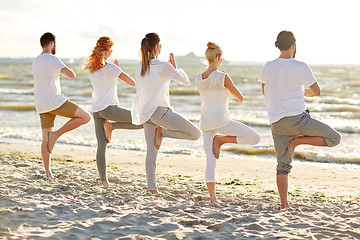 Image showing group of people making yoga in tree pose on beach