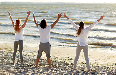 Image showing group of people making yoga or meditating on beach