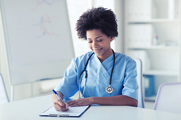 Image showing happy female doctor or nurse writing to clipboard