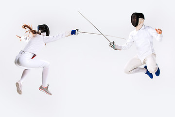 Image showing The woman and man wearing fencing suit practicing with sword against gray