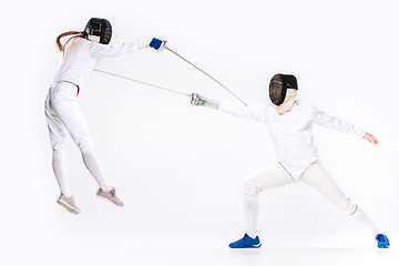 Image showing The woman and man wearing fencing suit practicing with sword against gray