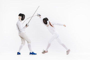 Image showing The woman and man wearing fencing suit practicing with sword against gray
