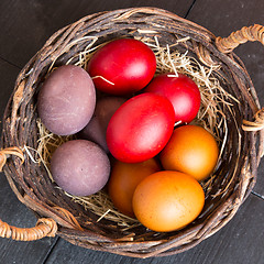 Image showing Wicker basket with colorful Easter eggs on wooden table.