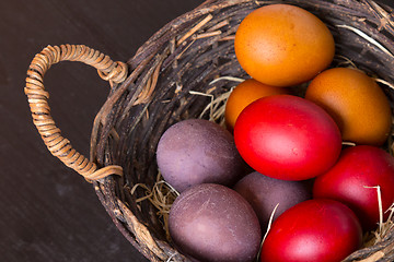 Image showing Wicker basket with colorful Easter eggs on wooden table.