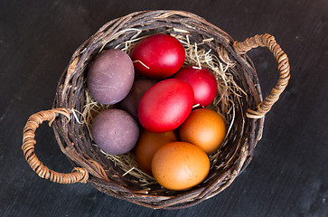 Image showing Wicker basket with colorful Easter eggs on wooden table.