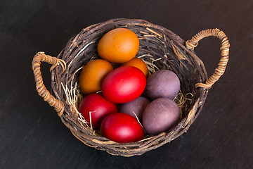 Image showing Wicker basket with colorful Easter eggs on wooden table.