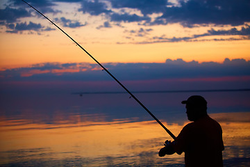 Image showing Silhouette of fishermen on quiet ocean with rays sunset