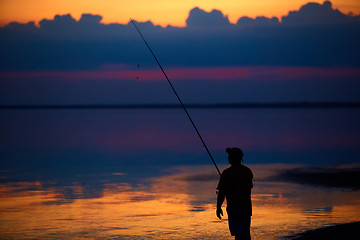 Image showing Silhouette of fishermen on quiet ocean with rays sunset