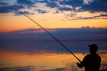 Image showing Silhouette of fishermen on quiet ocean with rays sunset