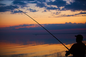 Image showing Silhouette of fishermen on quiet ocean with rays sunset