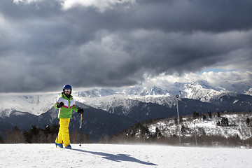 Image showing Young skier with ski poles in sun mountains and cloudy gray sky 