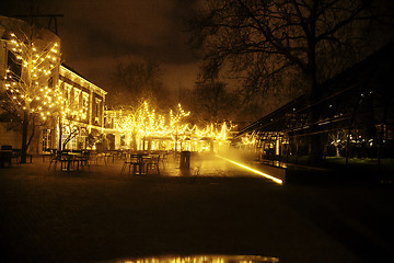 Image showing empty night restaurant, lot of tables and chairs with noone, magic fairy lights on trees like christmas celebration