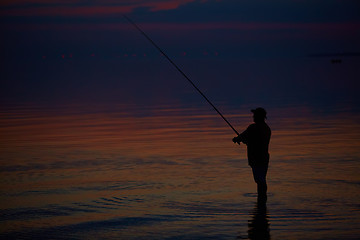 Image showing Silhouette of fishermen on quiet ocean with rays sunset