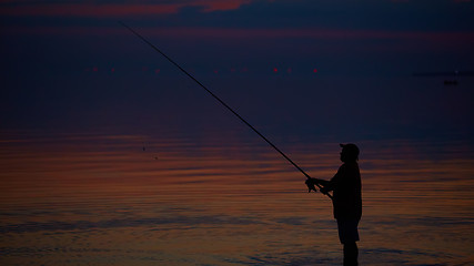 Image showing Silhouette of fishermen on quiet ocean with rays sunset