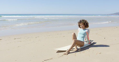 Image showing Young woman sitting on a surfboard