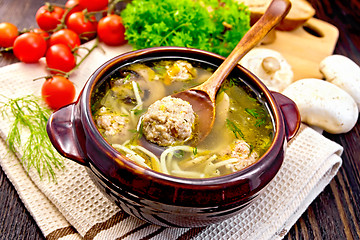 Image showing Soup with meatballs and spoon in clay bowl on board