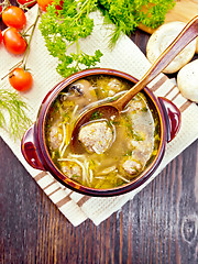 Image showing Soup with meatballs and spoon in clay bowl on board top