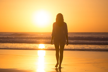 Image showing Lady walking on sandy beach in sunset.
