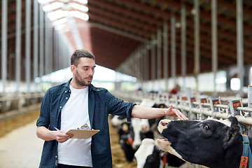 Image showing farmer with clipboard and cows in cowshed on farm