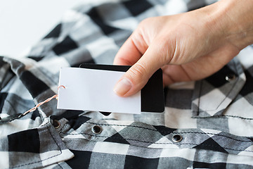 Image showing close up of hand holding checkered shirt price tag