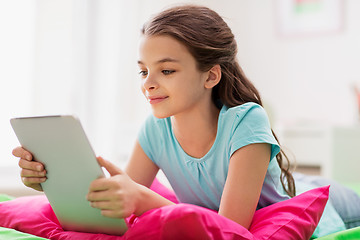 Image showing smiling girl with tablet pc lying in bed at home