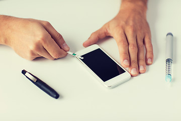 Image showing close up of man with smartphone making blood test