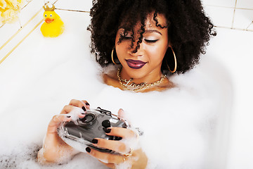 Image showing young afro-american teen girl laying in bath with foam, wearing 